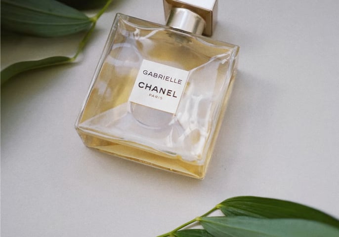 Gabrielle Chanel perfume bottle laying on a table with green leaves.